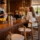 Elegancka lada barowa z drewna dębu z widocznymi słojami, bukowe hokery z tapicerką, barman czyszczący szklanki. Naturalne światło, prestiżowe wnętrze restauracji.