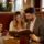Para siedzi w nowoczesnej restauracyjnej loży z premium tapicerką w kolorach brązu i złota, oświetlona naturalnym światłem, w eleganckim wnętrzu hotelu.